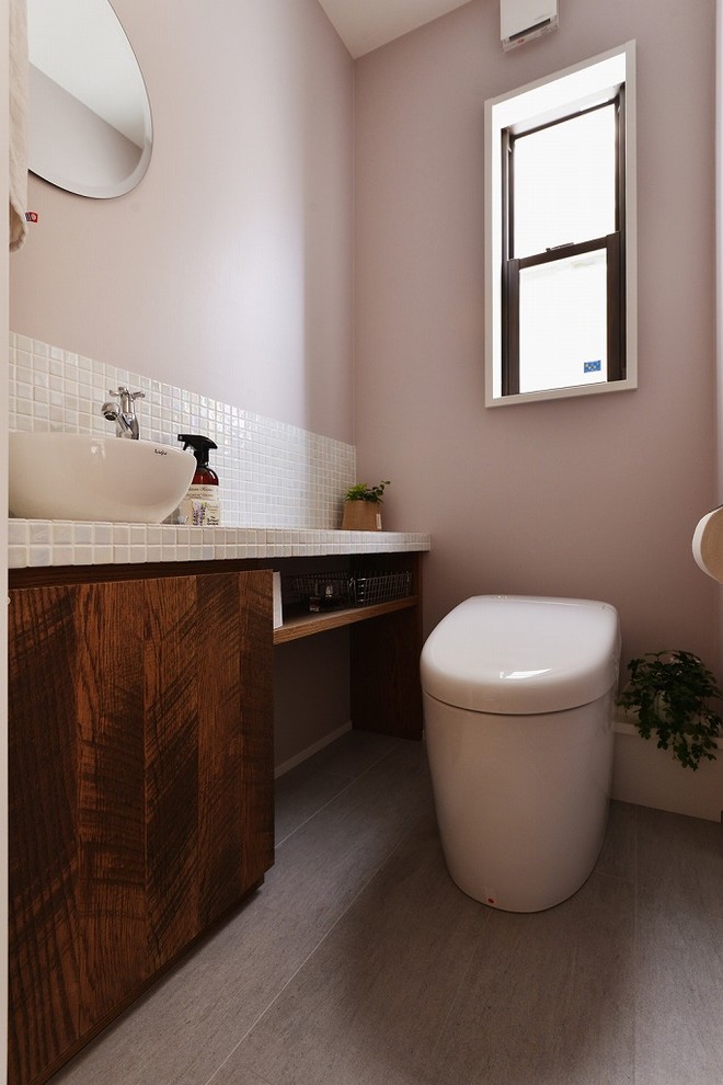 Contemporary powder room in Tokyo with flat-panel cabinets, medium wood cabinets, pink walls, a vessel sink and grey floor.