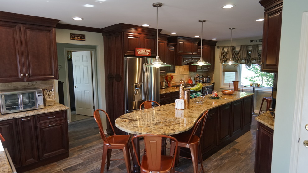Eat-in kitchen - large transitional l-shaped ceramic tile and brown floor eat-in kitchen idea in New York with an undermount sink, raised-panel cabinets, brown cabinets, granite countertops, beige backsplash, marble backsplash, stainless steel appliances and an island