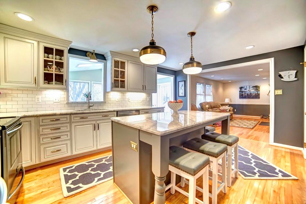 Enclosed kitchen - mid-sized transitional l-shaped light wood floor enclosed kitchen idea in Baltimore with a single-bowl sink, raised-panel cabinets, white cabinets, white backsplash, subway tile backsplash, stainless steel appliances and an island