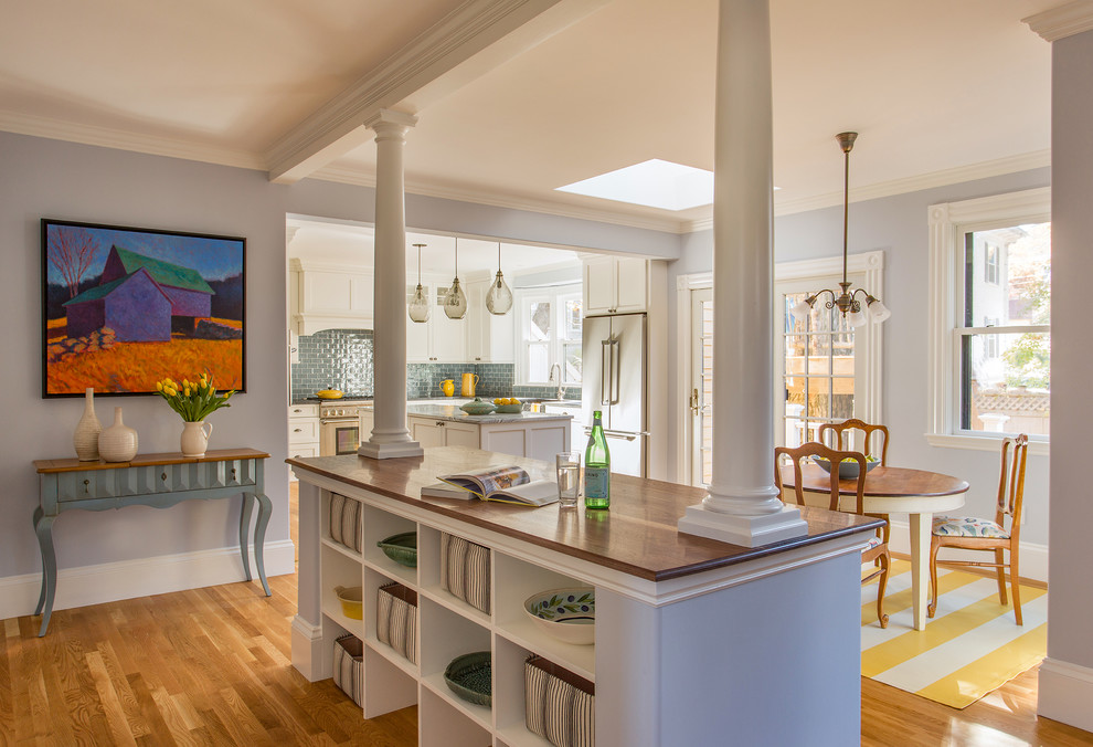 Photo of a large traditional l-shaped eat-in kitchen in Boston with a farmhouse sink, shaker cabinets, white cabinets, marble benchtops, blue splashback, glass tile splashback, stainless steel appliances, medium hardwood floors and multiple islands.