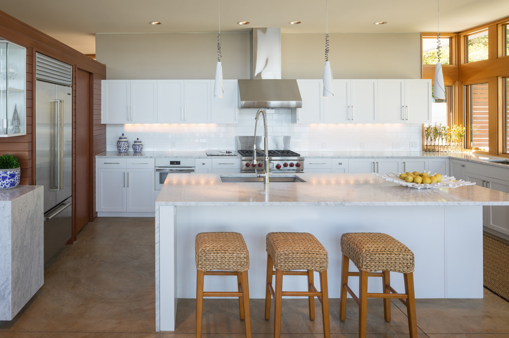 Large contemporary u-shaped open plan kitchen in Seattle with an undermount sink, recessed-panel cabinets, white cabinets, marble benchtops, white splashback, ceramic splashback, stainless steel appliances, concrete floors, with island, beige floor and white benchtop.
