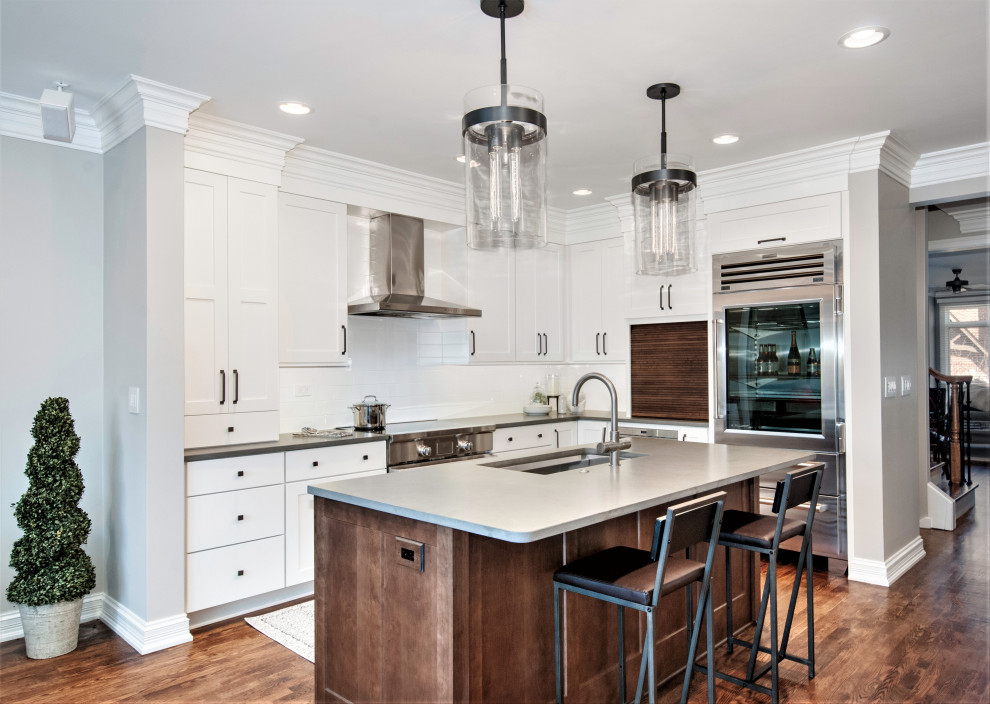 Inspiration for a mid-sized industrial l-shaped open plan kitchen in Chicago with an undermount sink, shaker cabinets, white cabinets, quartz benchtops, white splashback, ceramic splashback, stainless steel appliances, dark hardwood floors, with island, brown floor and grey benchtop.
