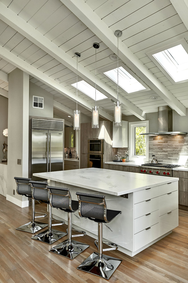 Inspiration for a large contemporary l-shaped open plan kitchen in San Francisco with an undermount sink, flat-panel cabinets, medium wood cabinets, quartzite benchtops, grey splashback, travertine splashback, stainless steel appliances, medium hardwood floors, with island, brown floor and white benchtop.