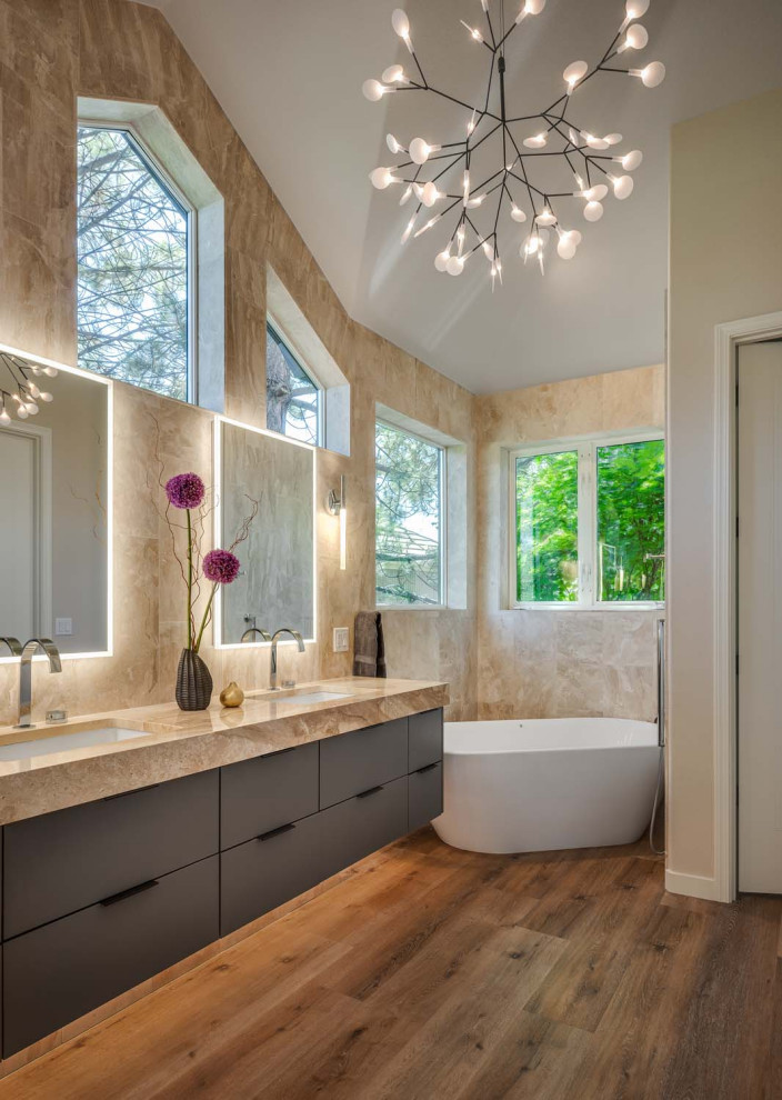 This is an example of a contemporary ensuite bathroom in Portland with flat-panel cabinets, grey cabinets, a freestanding bath, an alcove shower, beige tiles, marble tiles, beige walls, vinyl flooring, a submerged sink, marble worktops, a hinged door, beige worktops, double sinks, a floating vanity unit and a vaulted ceiling.