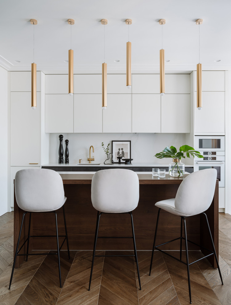 Mid-sized contemporary galley kitchen in Saint Petersburg with flat-panel cabinets, white cabinets, white appliances, medium hardwood floors, with island, brown floor and white benchtop.