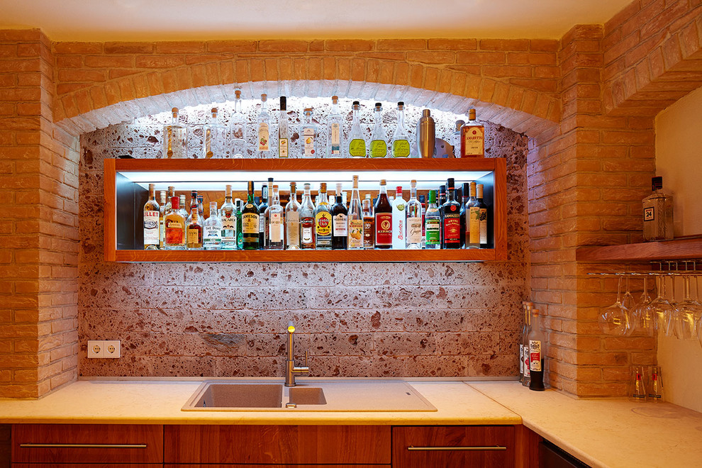 Design ideas for a mid-sized mediterranean l-shaped seated home bar in Munich with flat-panel cabinets, dark wood cabinets, concrete benchtops, brown splashback and stone tile splashback.