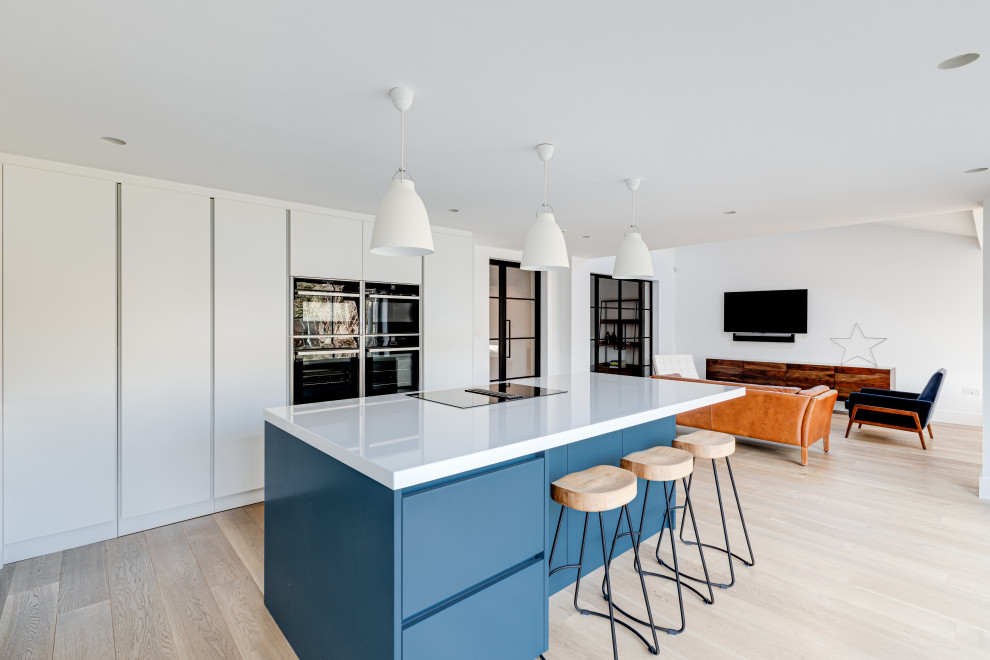 Expansive contemporary u-shaped eat-in kitchen in Hertfordshire with an integrated sink, flat-panel cabinets, white cabinets, quartzite benchtops, black splashback, metal splashback, black appliances, painted wood floors, with island, white floor and white benchtop.