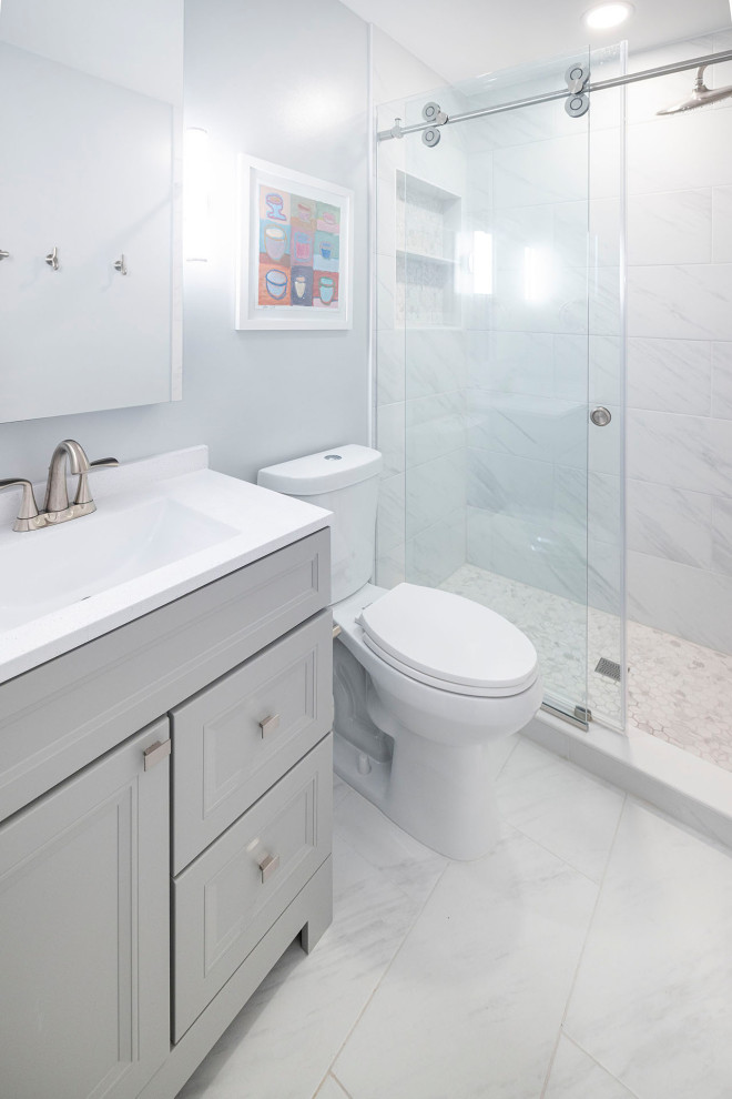 Cette image montre une petite douche en alcôve minimaliste avec un placard à porte shaker, des portes de placard grises, WC à poser, un carrelage blanc, des carreaux de porcelaine, un mur gris, un sol en carrelage de porcelaine, un lavabo intégré, un plan de toilette en surface solide, un sol blanc, une cabine de douche à porte coulissante, un plan de toilette blanc, une niche, meuble simple vasque et meuble-lavabo sur pied.