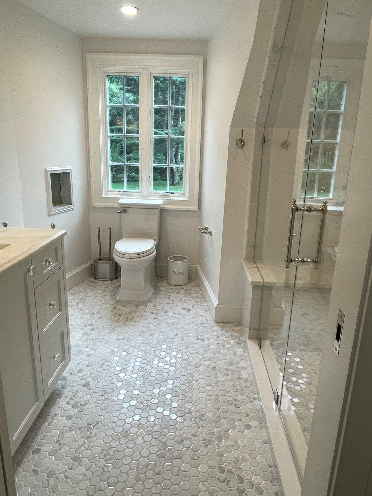 Teen Girl Bathroom - Example of a mid-sized transitional 3/4 medium tone wood floor, brown floor and single-sink alcove shower design in New York with beaded inset cabinets, white cabinets, a two-piece toilet, white walls, an undermount sink, marble countertops, a hinged shower door, white countertops and a built-in vanity