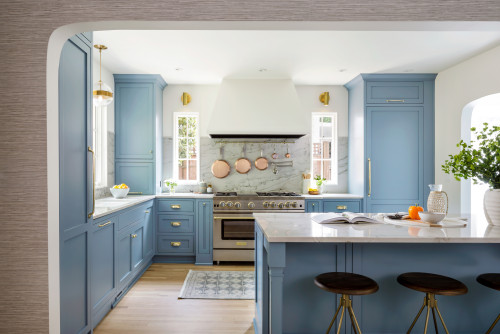 Light-filled kitchen with sky-blue RTA shaker cabinets, marble backsplash, white range hood, and a quartz island with three stools.