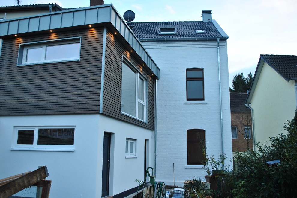 Photo of a small contemporary two-storey brown house exterior in Cologne with wood siding, a flat roof and a tile roof.