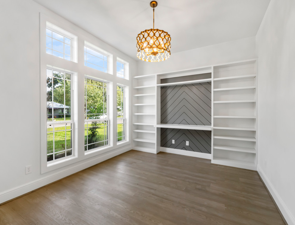 This is an example of a transitional study room in Houston with white walls, light hardwood floors, a built-in desk and planked wall panelling.