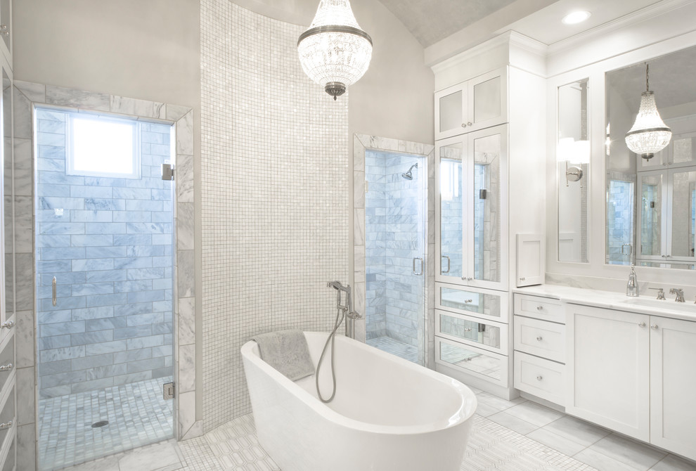 This is an example of a transitional master bathroom in Wichita with shaker cabinets, white cabinets, a freestanding tub, a double shower, gray tile, marble, grey walls, grey floor, a hinged shower door and white benchtops.