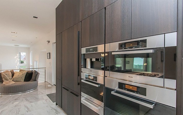 Photo of a large contemporary u-shaped open plan kitchen in Other with an integrated sink, flat-panel cabinets, dark wood cabinets, quartzite benchtops, grey splashback, glass sheet splashback, panelled appliances, marble floors and with island.