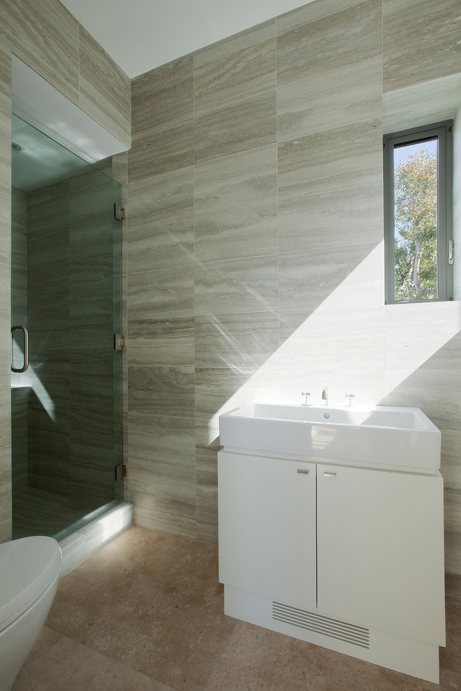 Photo of a large beach style master bathroom in Los Angeles with flat-panel cabinets, white cabinets, a freestanding tub, an alcove shower, a one-piece toilet, gray tile, cement tile, grey walls, limestone floors, a console sink, granite benchtops, beige floor, a hinged shower door and white benchtops.