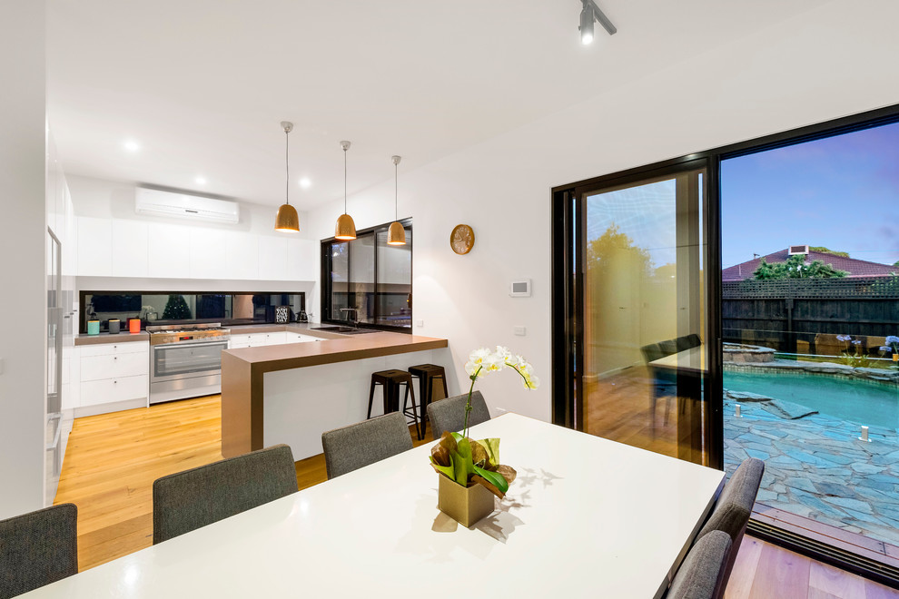 Inspiration for a mid-sized modern u-shaped eat-in kitchen in Melbourne with a double-bowl sink, stainless steel appliances, medium hardwood floors, no island, quartz benchtops and glass sheet splashback.