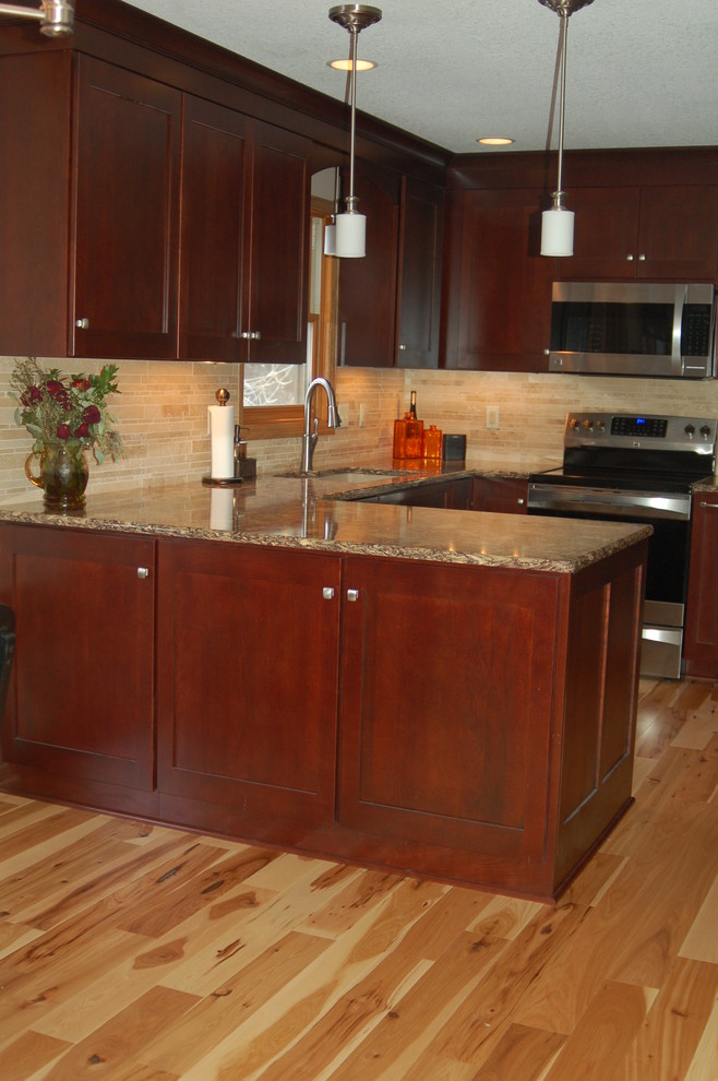This is an example of a mid-sized transitional u-shaped eat-in kitchen in Minneapolis with an undermount sink, recessed-panel cabinets, dark wood cabinets, quartz benchtops, beige splashback, stone tile splashback, stainless steel appliances, light hardwood floors and a peninsula.