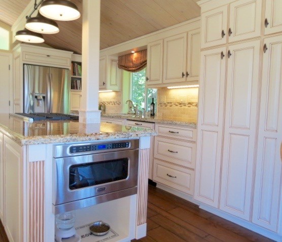 Photo of a mid-sized country galley open plan kitchen in Los Angeles with an undermount sink, raised-panel cabinets, beige cabinets, granite benchtops, beige splashback, stone tile splashback, stainless steel appliances, medium hardwood floors and with island.