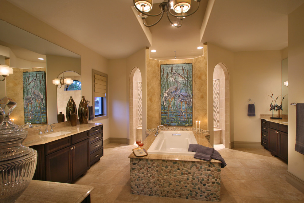 Large tropical master bathroom in Tampa with recessed-panel cabinets, dark wood cabinets, granite benchtops, a drop-in tub, an open shower, beige tile, pebble tile, beige walls, travertine floors, beige floor, an open shower and beige benchtops.