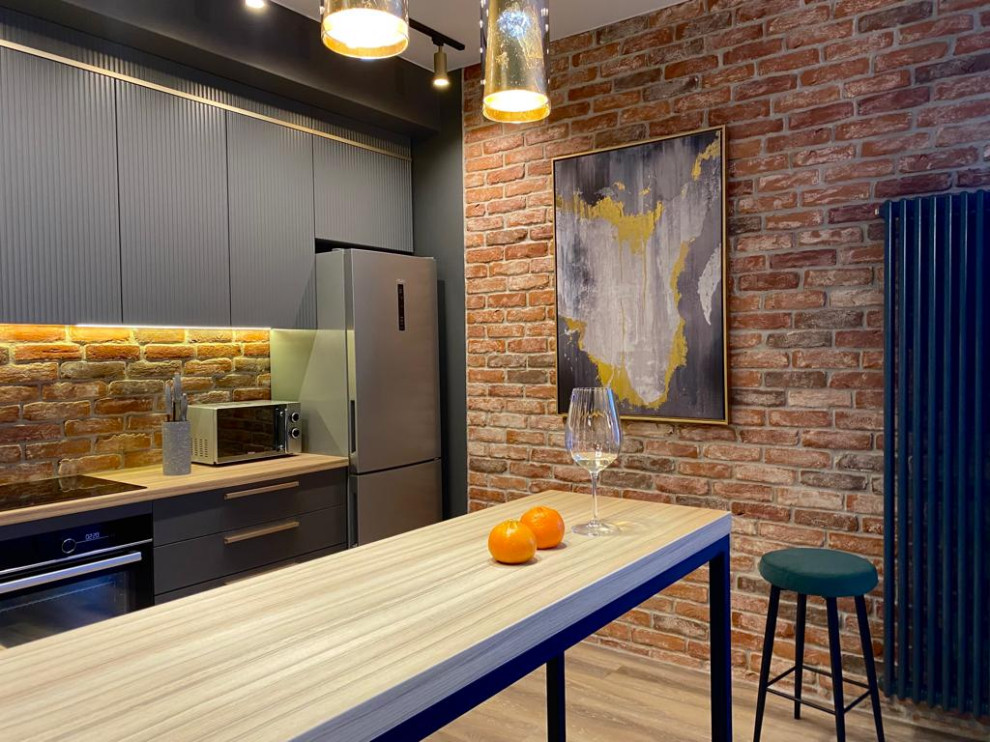 Photo of a mid-sized industrial l-shaped kitchen in Saint Petersburg with an undermount sink, flat-panel cabinets, grey cabinets, wood benchtops, brick splashback, stainless steel appliances, vinyl floors, a peninsula and beige benchtop.