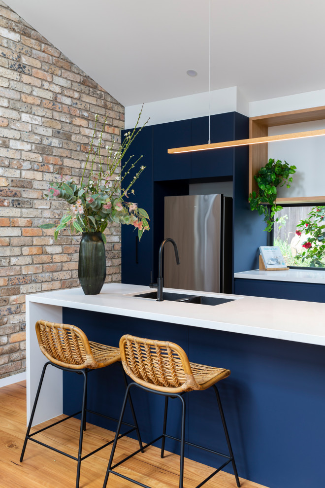 Inspiration for a mid-sized contemporary galley open plan kitchen in Canberra - Queanbeyan with an undermount sink, blue cabinets, quartz benchtops, window splashback, black appliances, medium hardwood floors, with island and white benchtop.