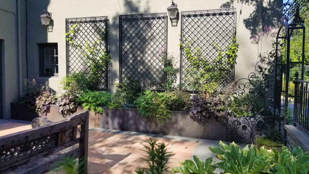 Ejemplo de jardín mediterráneo en verano en patio con jardín francés, macetero elevado, exposición parcial al sol, adoquines de piedra natural y con metal
