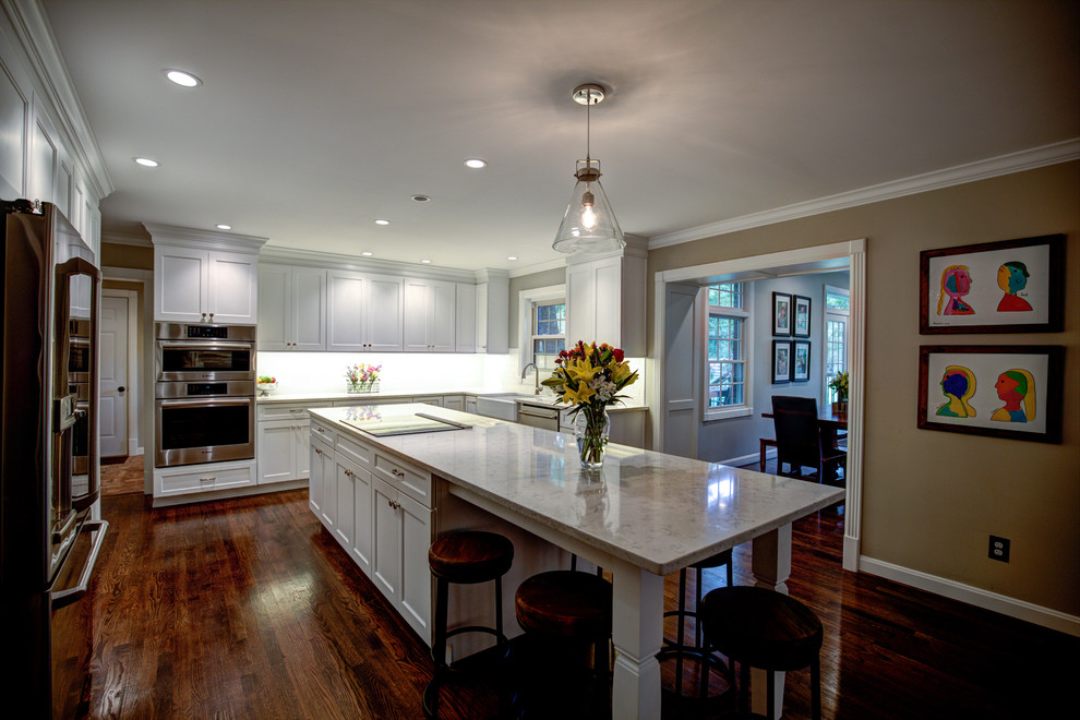 Inspiration for a large transitional medium tone wood floor kitchen remodel with a farmhouse sink, shaker cabinets, white cabinets, solid surface countertops, white backsplash, subway tile backsplash and stainless steel appliances