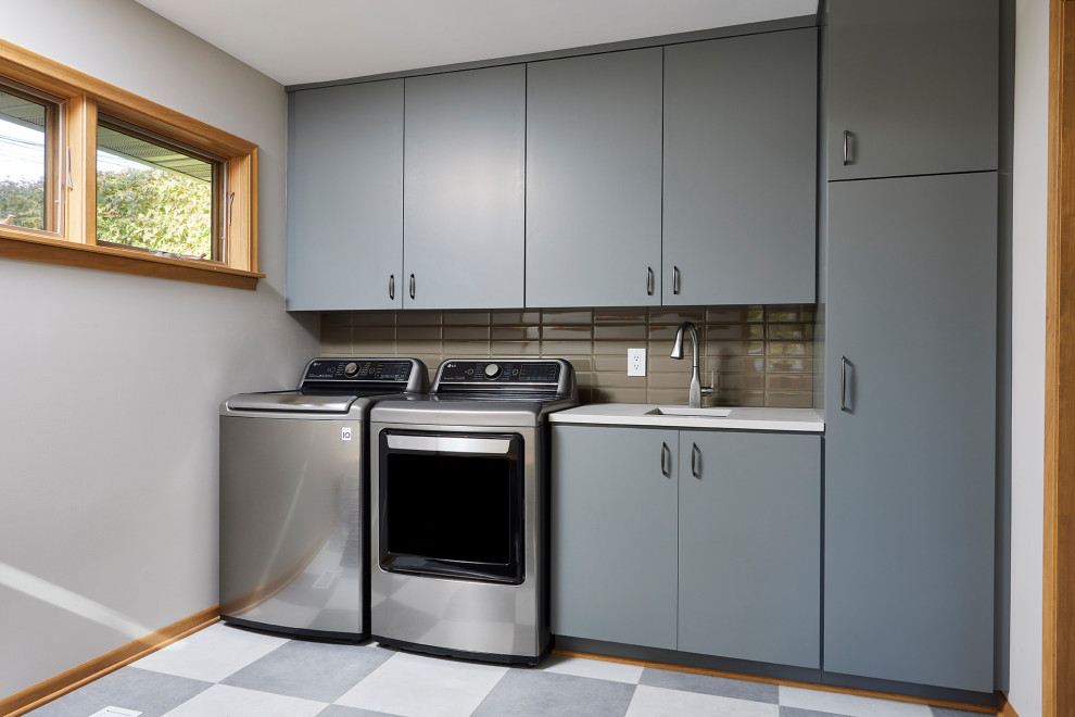 Design ideas for a mid-sized arts and crafts single-wall dedicated laundry room in Minneapolis with an undermount sink, flat-panel cabinets, grey cabinets, quartz benchtops, green splashback, beige walls, laminate floors, a side-by-side washer and dryer, multi-coloured floor and white benchtop.