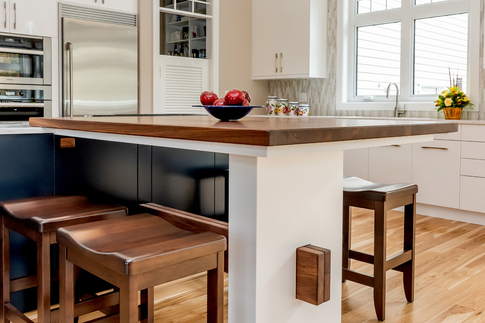 Kitchen pantry - large transitional l-shaped light wood floor and beige floor kitchen pantry idea with a double-bowl sink, flat-panel cabinets, white cabinets, quartz countertops, gray backsplash, cement tile backsplash, stainless steel appliances, an island and white countertops