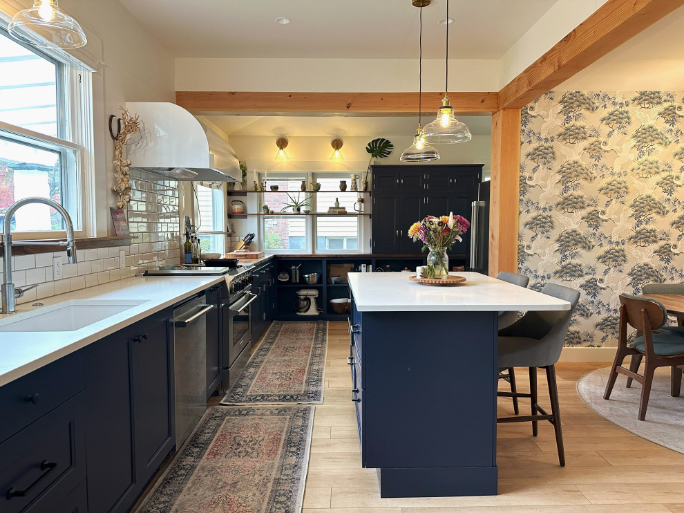 Inredning av ett klassiskt mellanstort vit vitt kök, med en undermonterad diskho, luckor med infälld panel, blå skåp, bänkskiva i kvarts, vitt stänkskydd, stänkskydd i tunnelbanekakel, rostfria vitvaror, ljust trägolv, en köksö och beiget golv
