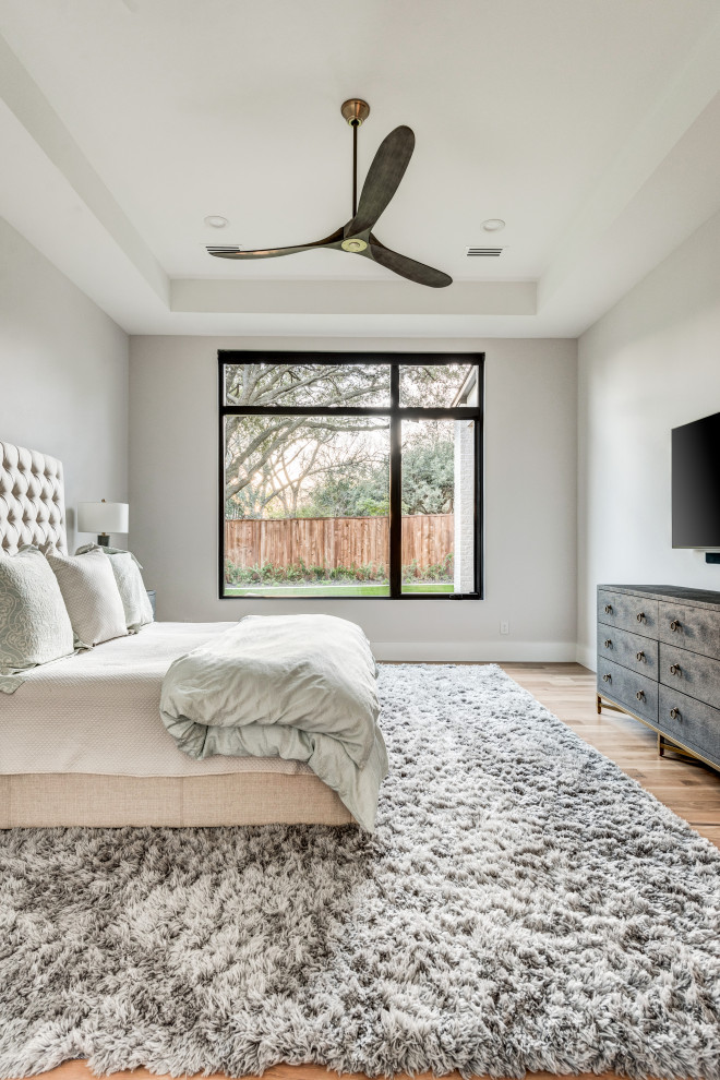 This is an example of a large transitional master bedroom in Dallas with grey walls, medium hardwood floors and beige floor.