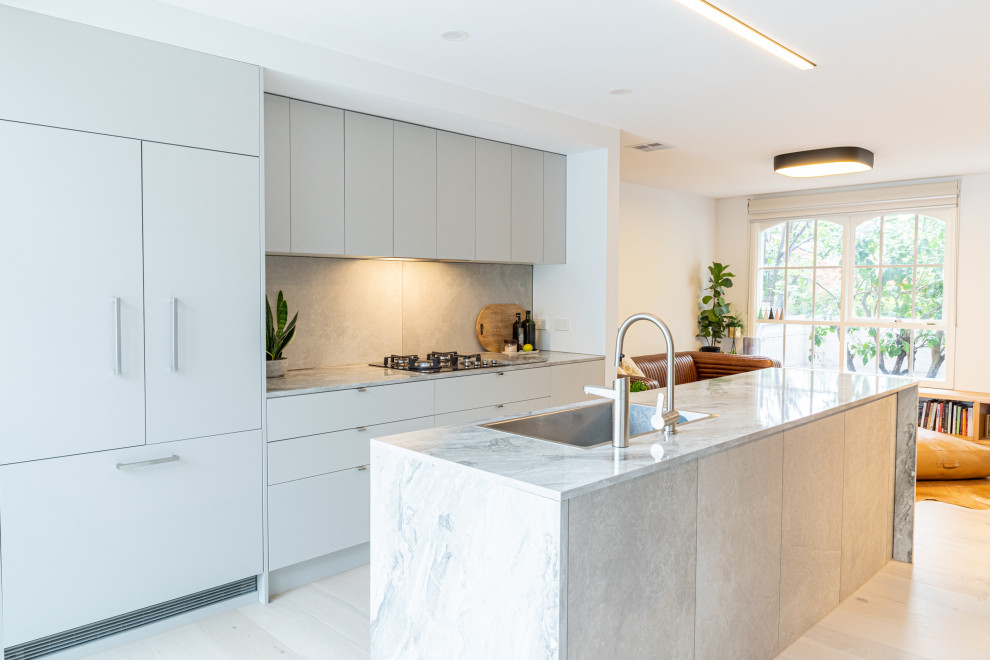 Photo of a contemporary galley kitchen in Melbourne with a drop-in sink, flat-panel cabinets, grey cabinets, panelled appliances, with island, beige floor and grey benchtop.