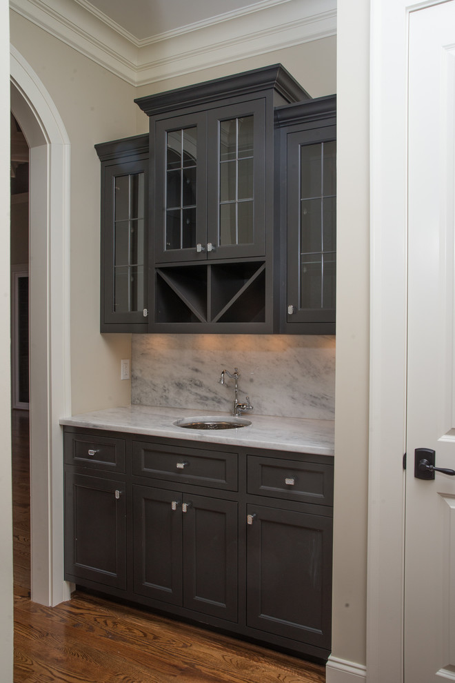Inspiration for a transitional wet bar in Other with an undermount sink, recessed-panel cabinets, black cabinets, marble benchtops, white splashback, stone slab splashback and medium hardwood floors.