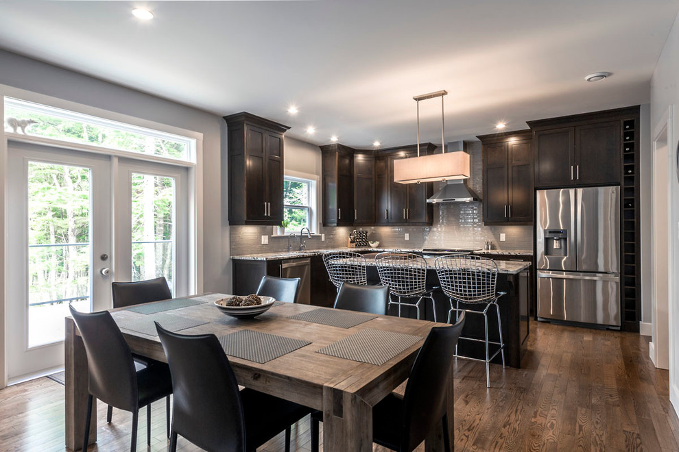 Example of a mid-sized transitional l-shaped medium tone wood floor and brown floor eat-in kitchen design with an undermount sink, shaker cabinets, dark wood cabinets, granite countertops, gray backsplash, glass tile backsplash, stainless steel appliances and an island