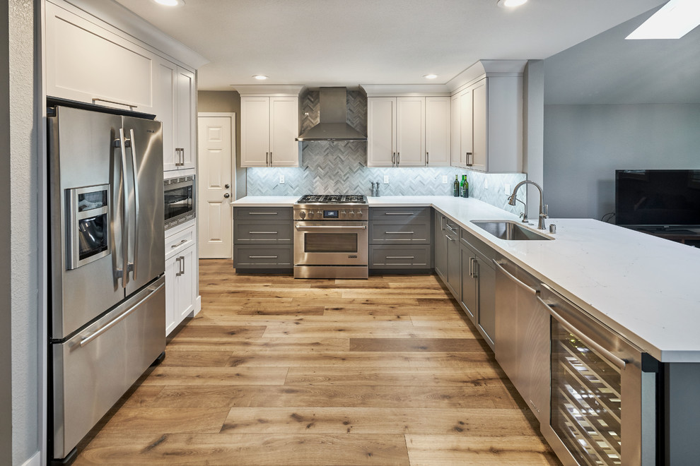 Example of a small transitional u-shaped medium tone wood floor eat-in kitchen design in San Francisco with an undermount sink, shaker cabinets, white cabinets, quartz countertops, gray backsplash, stone tile backsplash, stainless steel appliances and a peninsula