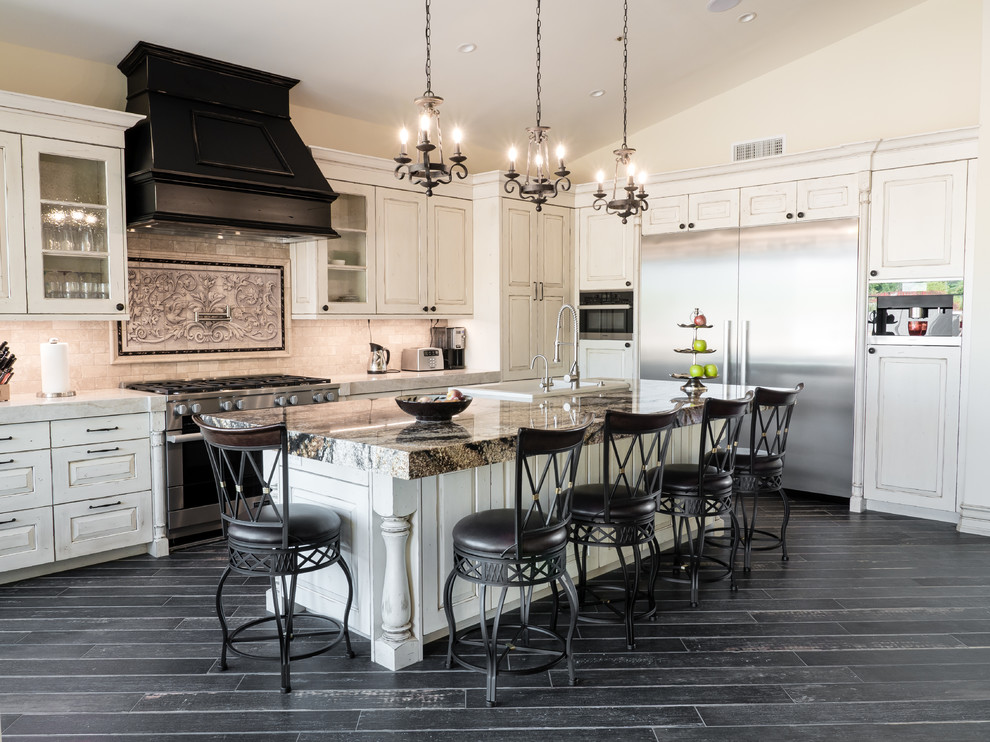 This is an example of a large traditional l-shaped open plan kitchen in Phoenix with a farmhouse sink, raised-panel cabinets, white cabinets, granite benchtops, beige splashback, stone tile splashback, stainless steel appliances, porcelain floors, with island and black floor.