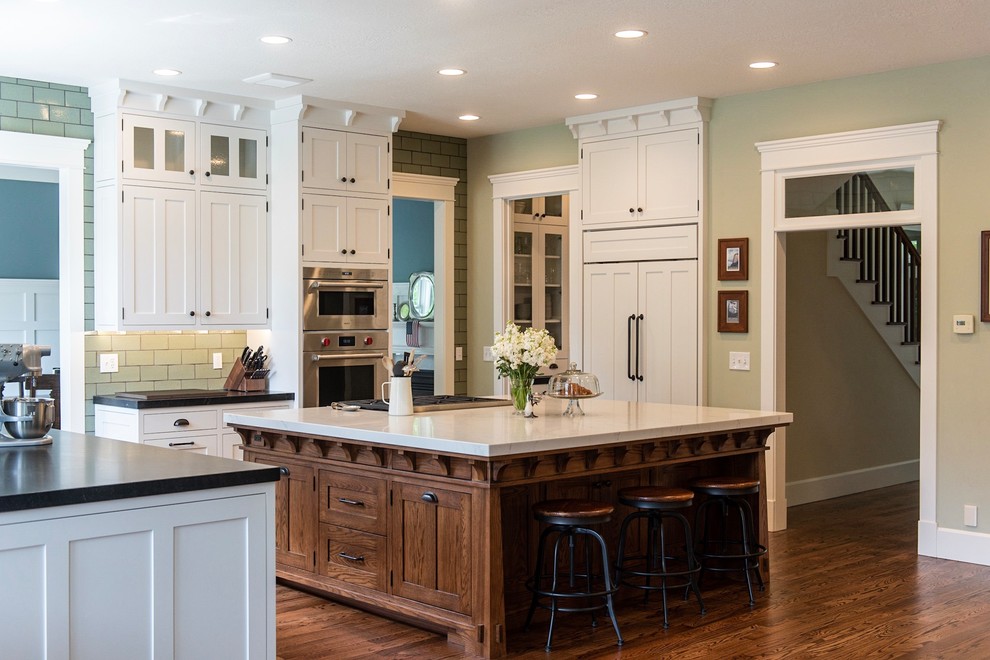 Photo of an arts and crafts u-shaped kitchen in Salt Lake City with shaker cabinets, with island, white cabinets, green splashback, panelled appliances, dark hardwood floors, brown floor and black benchtop.