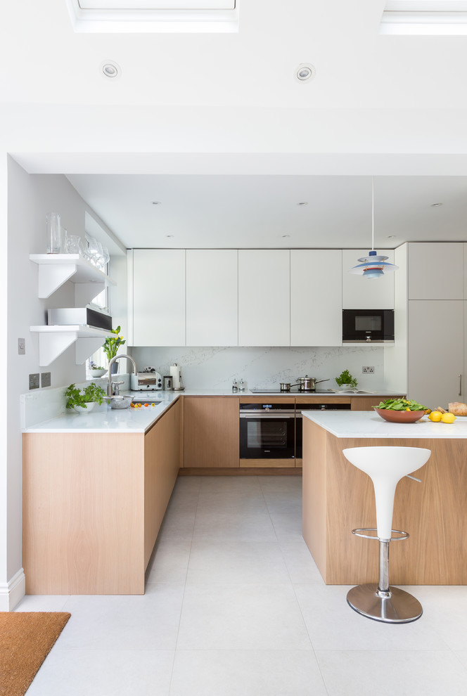 This is an example of a scandinavian l-shaped kitchen in London with an undermount sink, flat-panel cabinets, white cabinets, white splashback, black appliances, with island, white floor and white benchtop.