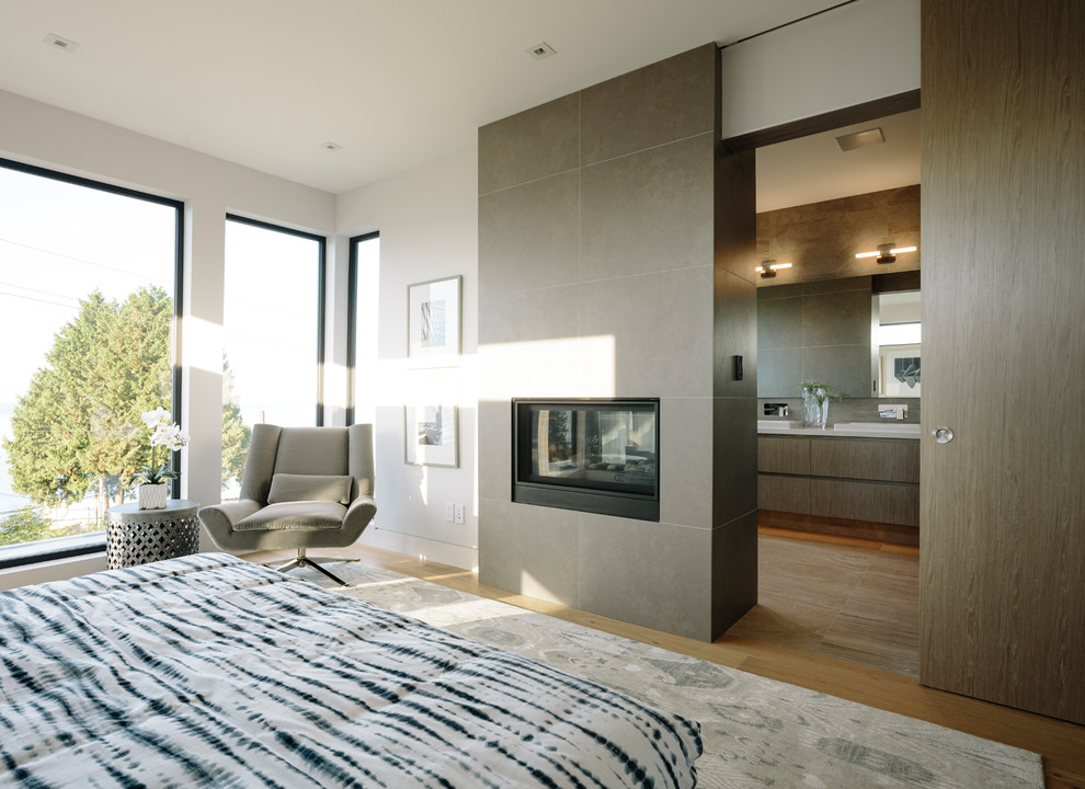 Photo of a large contemporary master bedroom in Vancouver with white walls, medium hardwood floors, a two-sided fireplace and a tile fireplace surround.