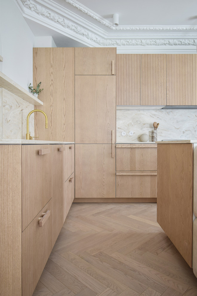 This is an example of a large contemporary l-shaped open plan kitchen in Paris with an integrated sink, flat-panel cabinets, light wood cabinets, marble benchtops, beige splashback, marble splashback, panelled appliances, light hardwood floors, with island, beige floor and beige benchtop.