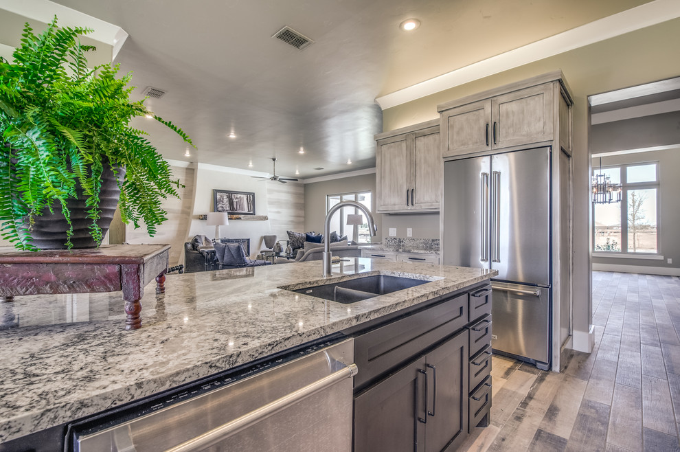 This is an example of a large transitional l-shaped eat-in kitchen in Austin with a single-bowl sink, shaker cabinets, grey cabinets, granite benchtops, grey splashback, matchstick tile splashback, stainless steel appliances, porcelain floors, with island and grey floor.