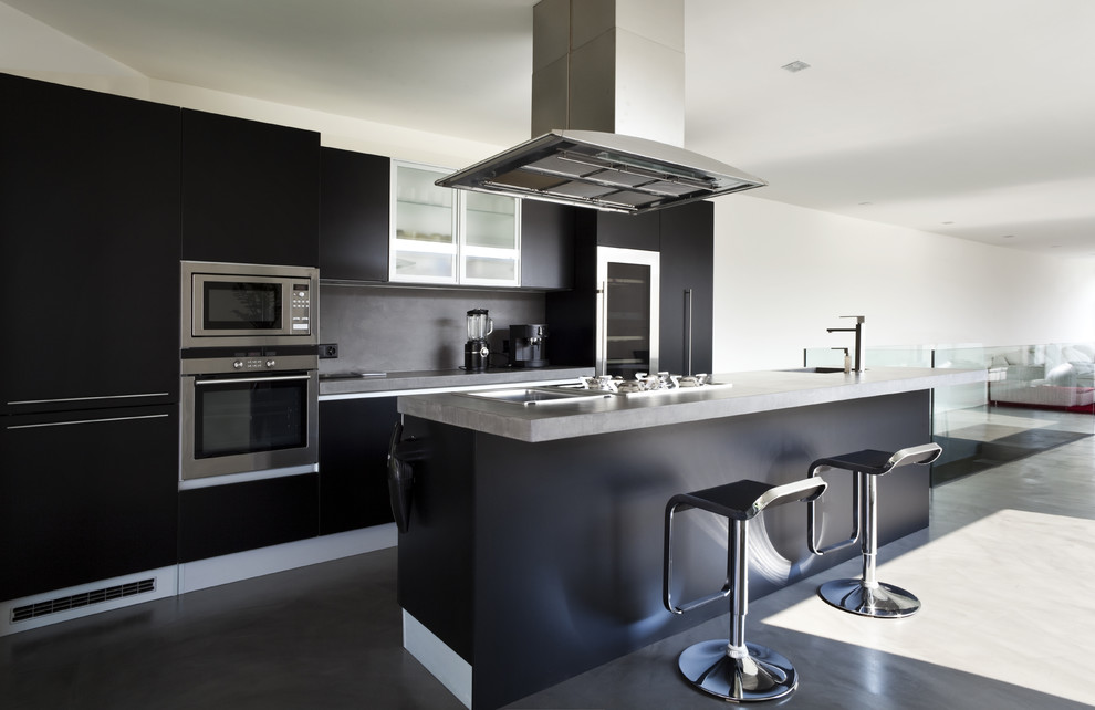 Contemporary galley kitchen in Other with flat-panel cabinets, black cabinets, grey splashback, stainless steel appliances, concrete floors and with island.