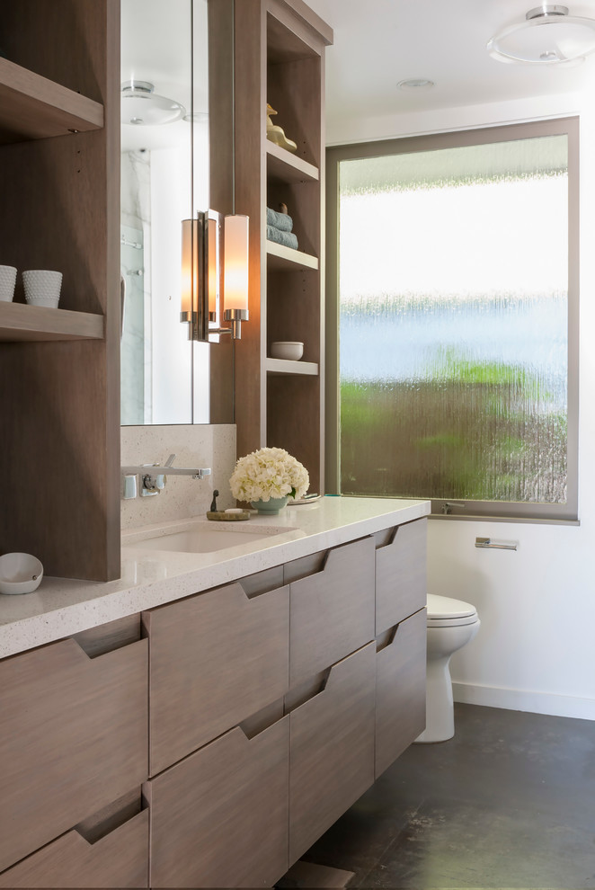 Photo of a small midcentury 3/4 bathroom in San Francisco with an undermount sink, flat-panel cabinets, medium wood cabinets, engineered quartz benchtops, an alcove tub, a shower/bathtub combo, a one-piece toilet, stone slab, white walls and concrete floors.