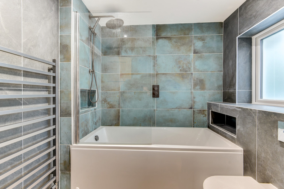 Photo of a medium sized modern grey and teal family bathroom in Sussex with flat-panel cabinets, grey cabinets, an alcove bath, a shower/bath combination, a one-piece toilet, grey tiles, ceramic tiles, grey walls, light hardwood flooring, a built-in sink, brown floors, a hinged door, feature lighting, a single sink and a floating vanity unit.