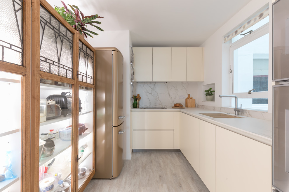 This is an example of a small contemporary galley separate kitchen in Sussex with no island, an undermount sink, flat-panel cabinets, white cabinets, white splashback, stone slab splashback, coloured appliances, beige floor and white benchtop.