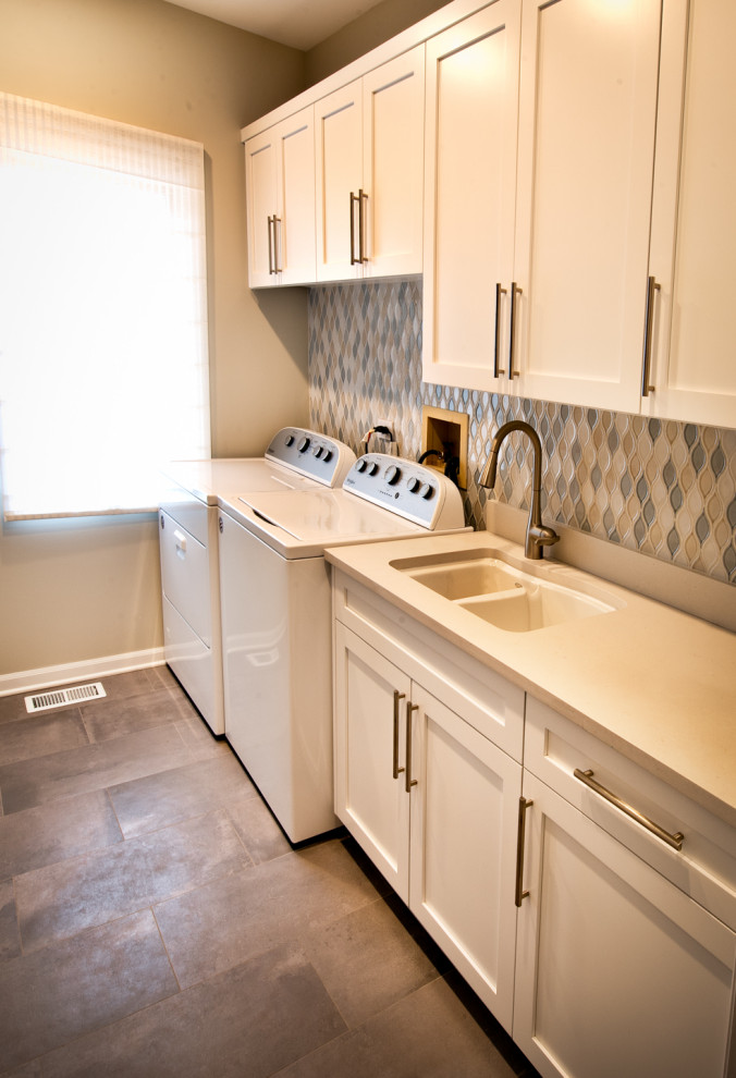 シカゴにある中くらいなモダンスタイルのおしゃれなランドリークローゼット (ドロップインシンク、シェーカースタイル扉のキャビネット、白いキャビネット、コンクリートカウンター、青いキッチンパネル、磁器タイルのキッチンパネル、ベージュの壁、コンクリートの床、左右配置の洗濯機・乾燥機、茶色い床、白いキッチンカウンター) の写真