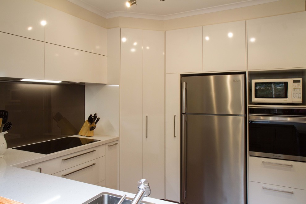 Photo of a mid-sized contemporary u-shaped separate kitchen in Melbourne with a drop-in sink, flat-panel cabinets, white cabinets, quartz benchtops, white splashback, glass sheet splashback, stainless steel appliances, medium hardwood floors and a peninsula.