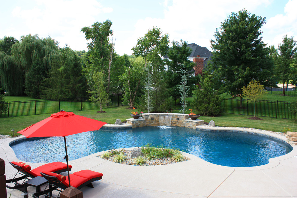 Photo of a large traditional backyard custom-shaped pool in St Louis with a water feature and concrete slab.
