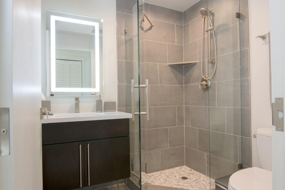This is an example of a small modern 3/4 bathroom in San Diego with flat-panel cabinets, dark wood cabinets, a corner shower, a two-piece toilet, gray tile, porcelain tile, white walls, porcelain floors, an undermount sink, solid surface benchtops, grey floor and a hinged shower door.