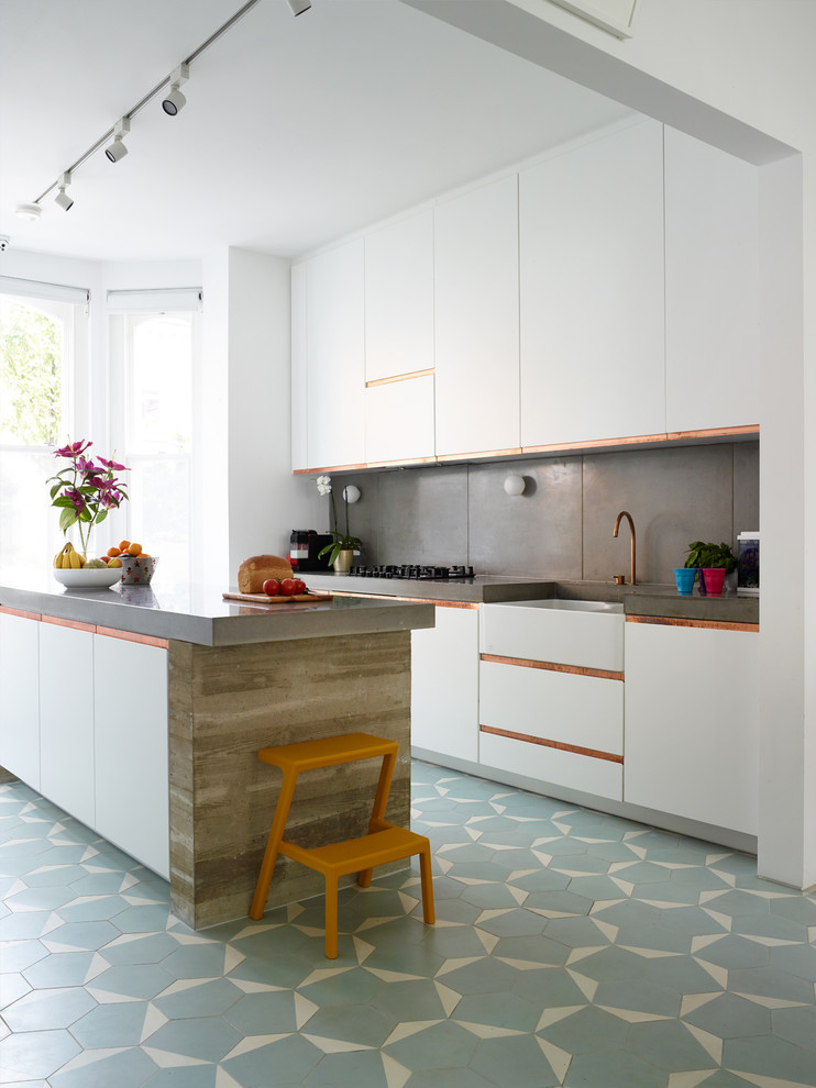 Large contemporary single-wall open plan kitchen in London with concrete benchtops, grey splashback, with island, a farmhouse sink, flat-panel cabinets, white cabinets, cement tile splashback and blue floor.